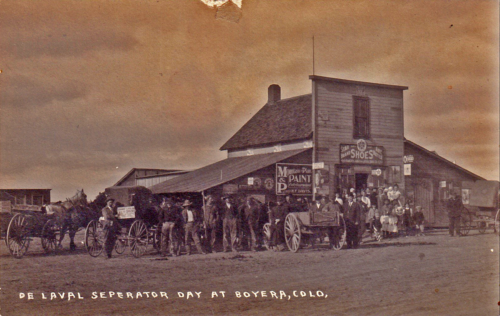 Historic photograph of residents gathered for De Laval Separator Day in Boyero, Colorado, early 1900s, showing horse-drawn wagons and storefronts including Star Brand Shoes and Mountain Plains Paint.